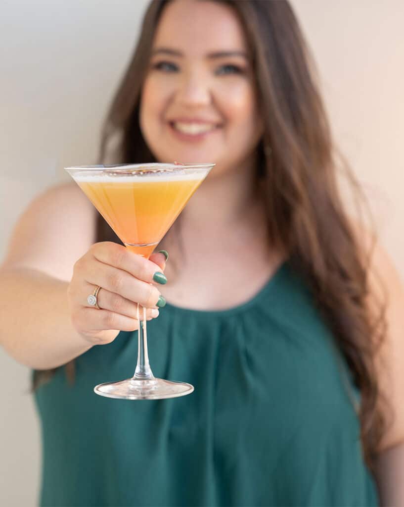 confident woman brand and website designer Victoria Galleguillos holding a passionfruit cocktail to the camera