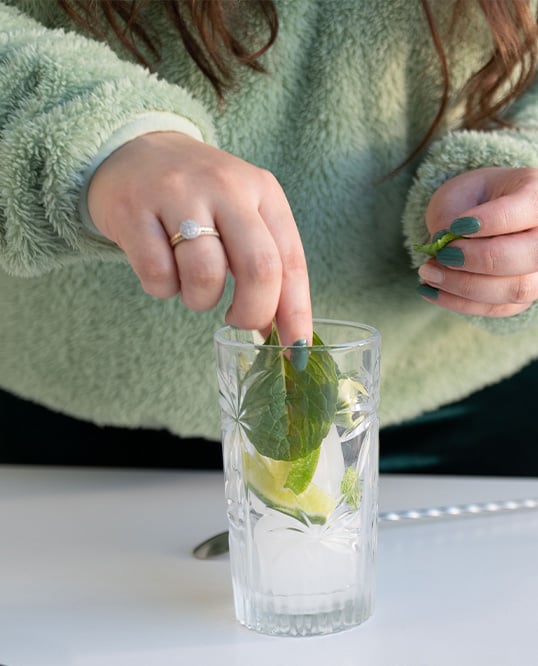 close up of a woman making a mojito cocktail, adding mint leaves on the glass