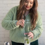 graphic designer mixing a mojito cocktail on a white table and a white brick wall in the background