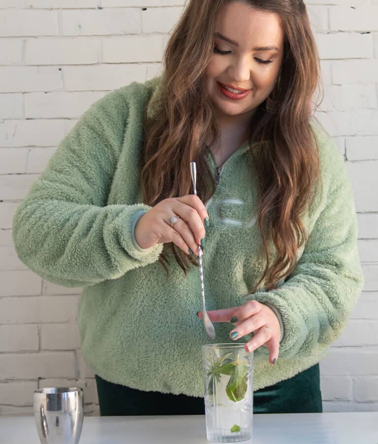 graphic designer mixing a mojito cocktail on a white table and a white brick wall in the background