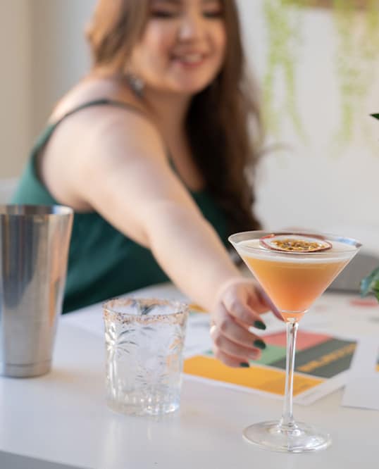 graphic designer photoshoot in the background trying to get a passionfruit cocktail on a white desk