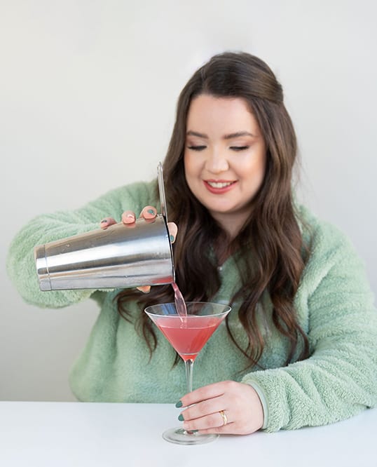 smiling woman pouring a cosmopolitan in a glass cocktails