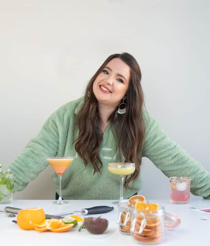 woman graphic designer smiling with some cocktails prepared on a table and fresh fruits